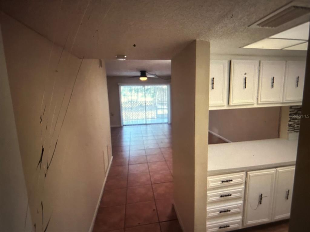 A view from a kitchen with white cabinets looking toward a tiled living area — 3425 TRICON LANE UNIT 12, HOLIDAY, FL