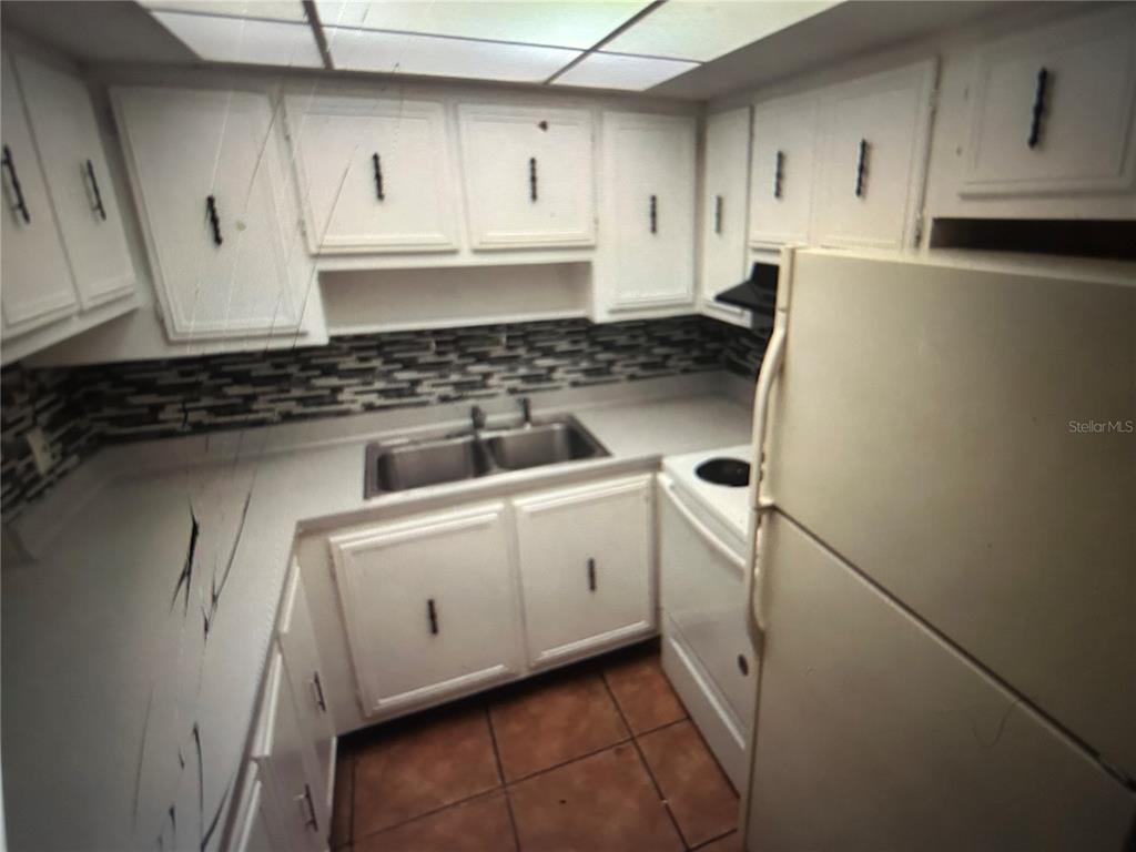 A galley-style kitchen features white cabinets, a double-basin sink, and a tiled backsplash — 3425 TRICON LANE UNIT 12, HOLIDAY, FL