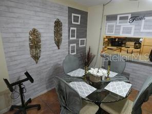 A dining area features a glass table, four gray chairs, and a wood-paneled accent wall — 3425 TRICON LANE UNIT 12, HOLIDAY, FL
