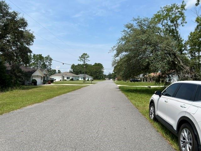 A paved residential street leads toward several houses under a blue sky with scattered trees — Lot 2 SW 132 STREET, OCALA, FL