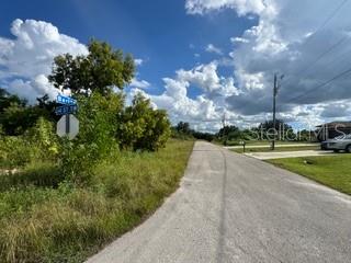 A paved road leads toward a street sign at a grassy intersection under a cloudy sky — 3913 14TH STREET SW, LEHIGH ACRES, FL