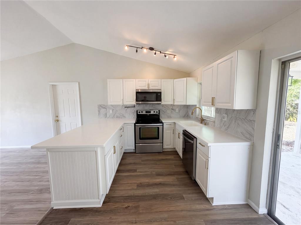 A kitchen features white cabinets, stainless steel appliances, marble-look backsplash, and a peninsula island — 3130 LUDLOW DRIVE, NEW PORT RICHEY, FL