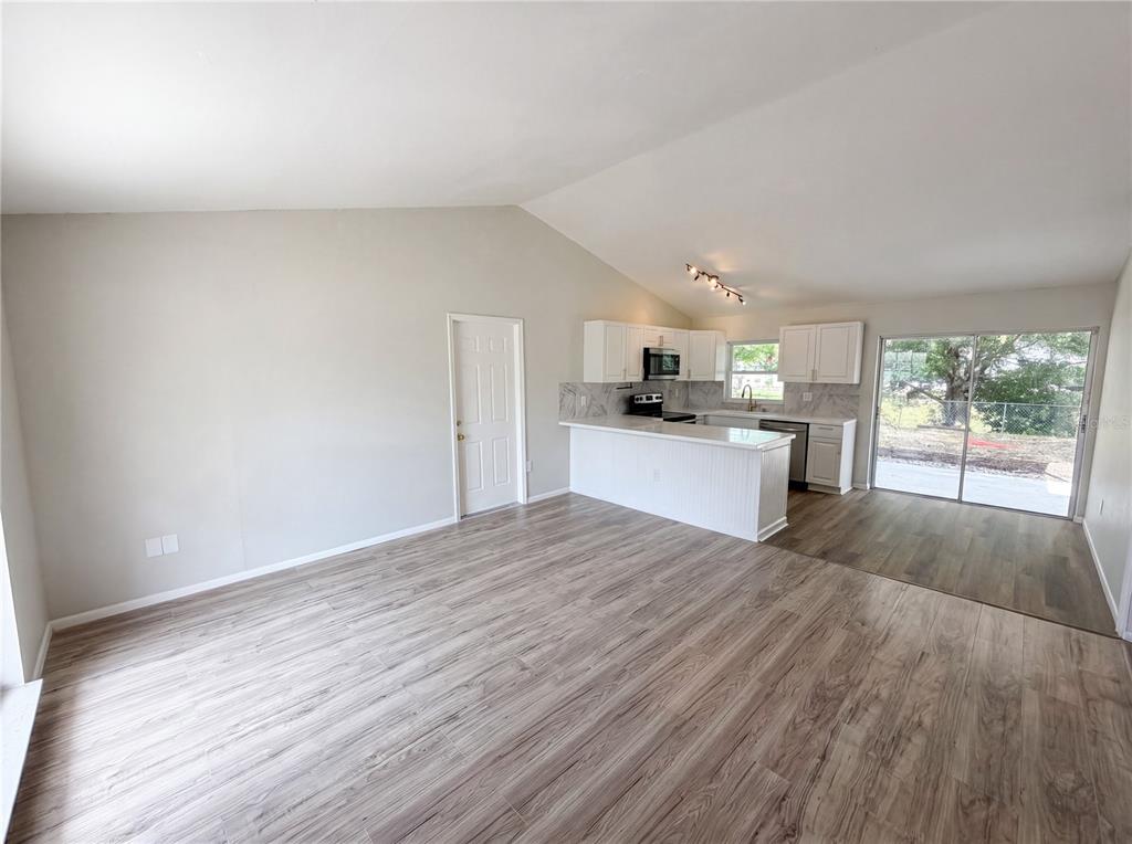 An open-concept living room and kitchen featuring light wood-look flooring and a vaulted ceiling — 3130 LUDLOW DRIVE, NEW PORT RICHEY, FL