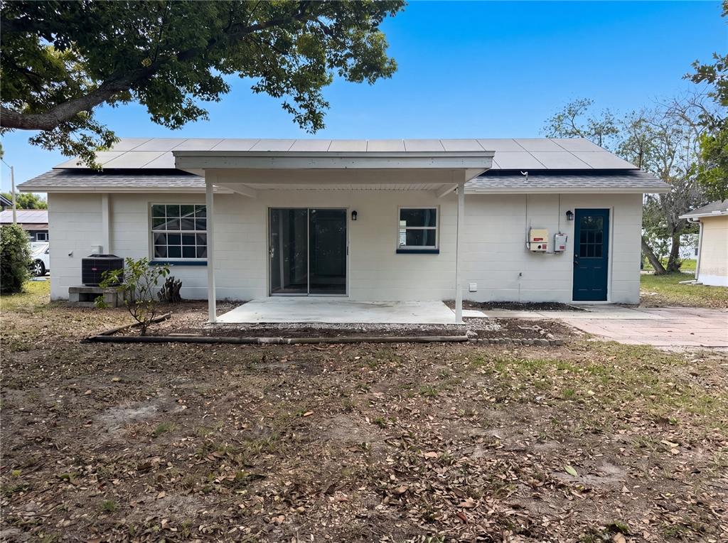 The rear exterior of a white house features a covered patio, sliding doors, and solar panels — 3130 LUDLOW DRIVE, NEW PORT RICHEY, FL