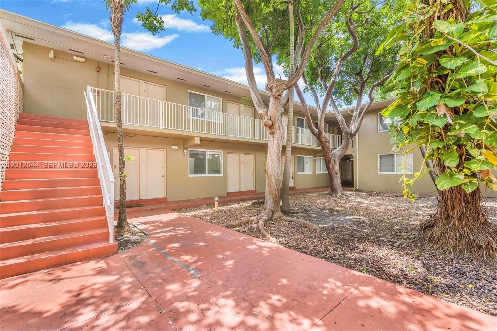 An exterior view of a two-story apartment building with orange stairs and a courtyard — 6330 SW 79th St # 2, South Miami FL 33143, SOUTH MIAMI, FL