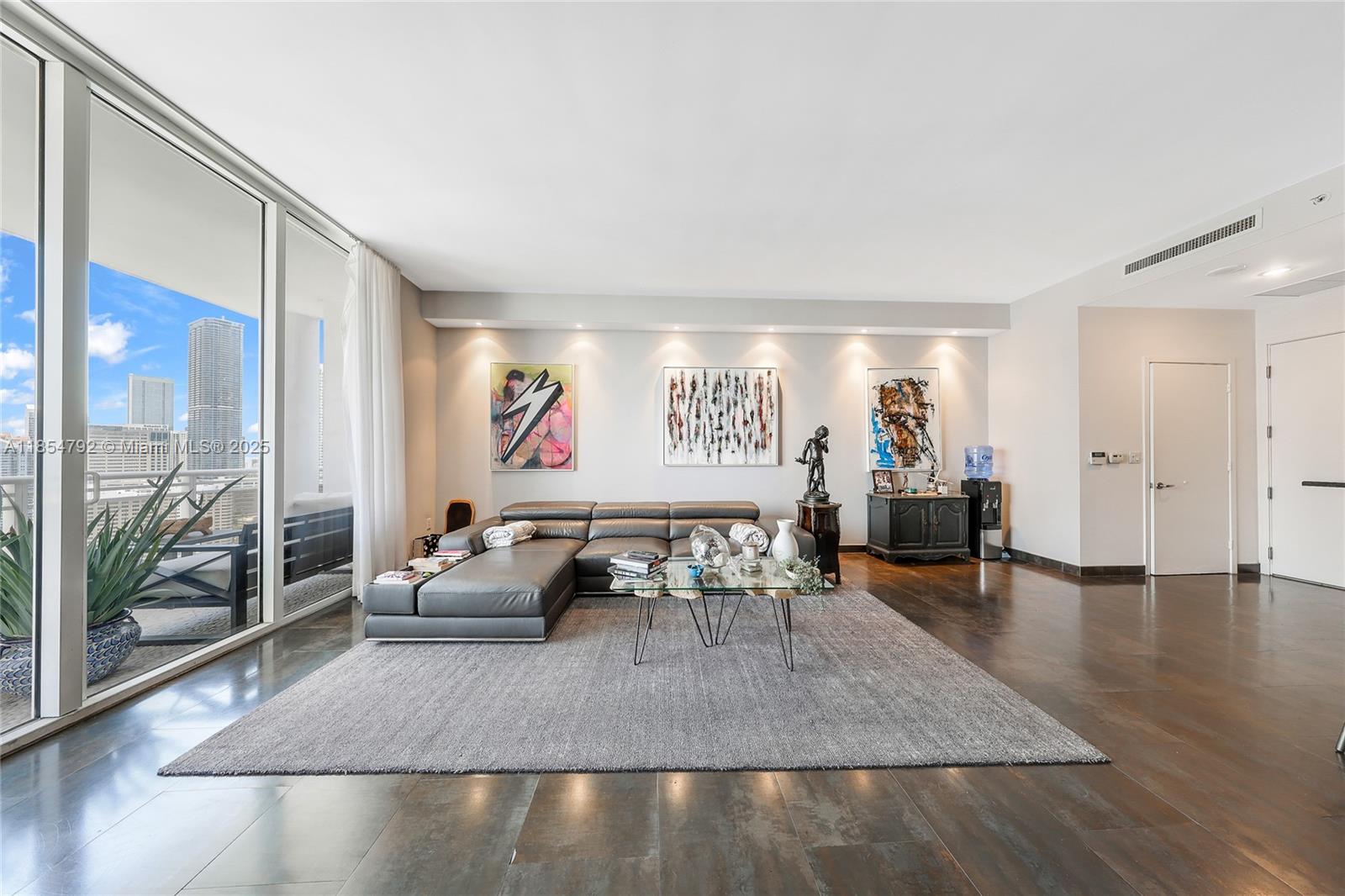 A modern living room features a grey sectional sofa, area rug, and floor-to-ceiling windows — 901 Brickell Key Blvd # 3002, Miami FL 33131, MIAMI, FL