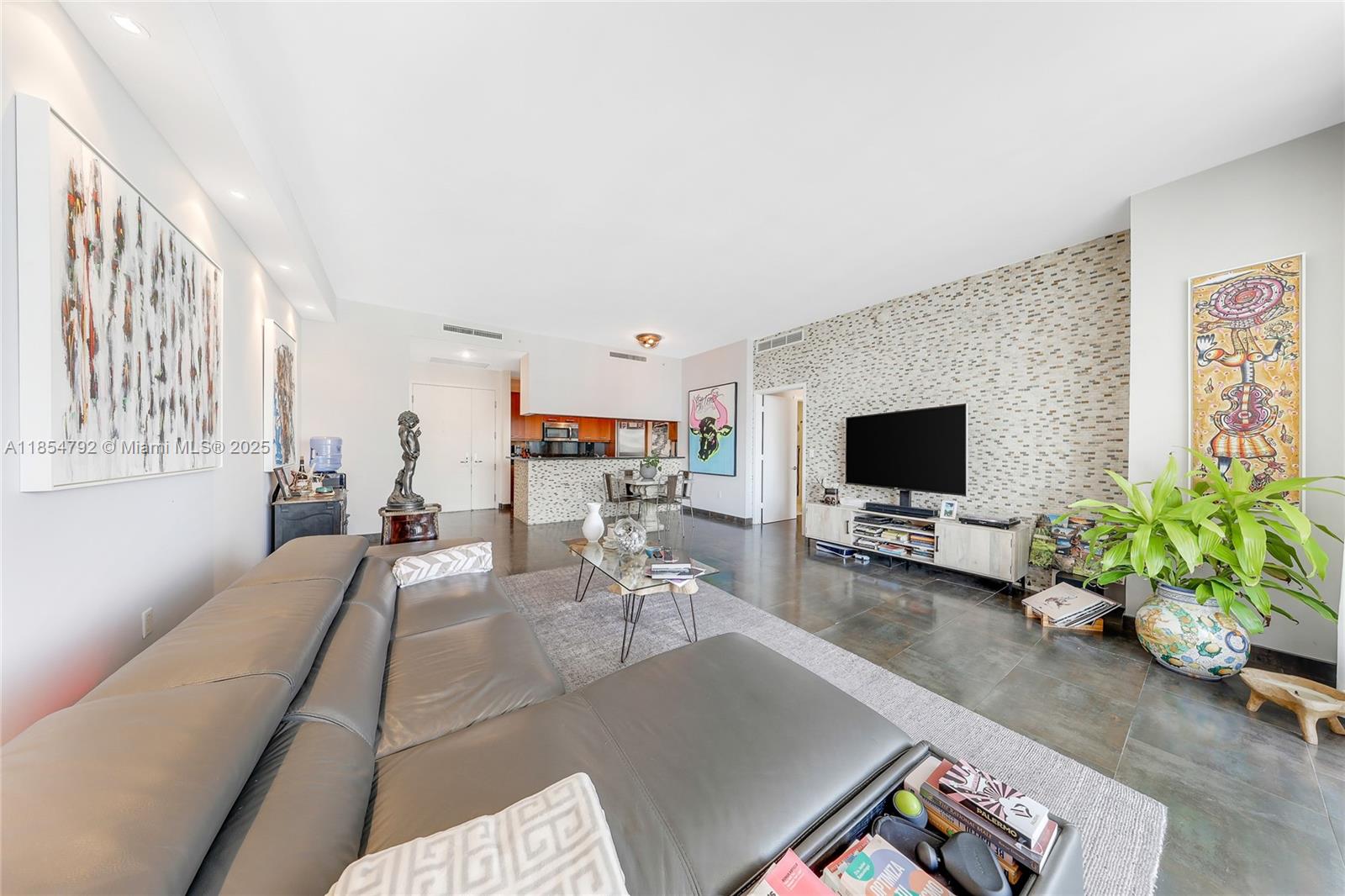 A modern living room features a large grey sectional sofa, a stone-tiled accent wall, and artwork — 901 Brickell Key Blvd # 3002, Miami FL 33131, MIAMI, FL