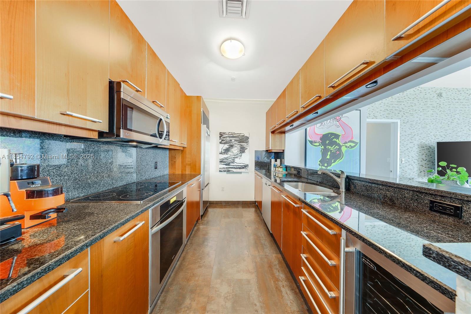 A galley kitchen features wood cabinetry, dark granite countertops, and stainless steel appliances — 901 Brickell Key Blvd # 3002, Miami FL 33131, MIAMI, FL