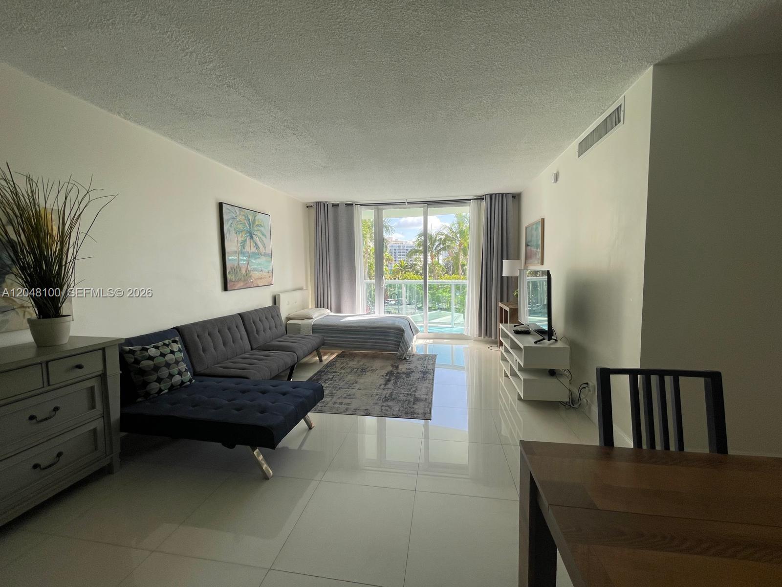 A living room with a sofa, bed, and balcony view features white tile flooring — 3901 S Ocean Dr # 3U, Hollywood FL 33019, HOLLYWOOD, FL