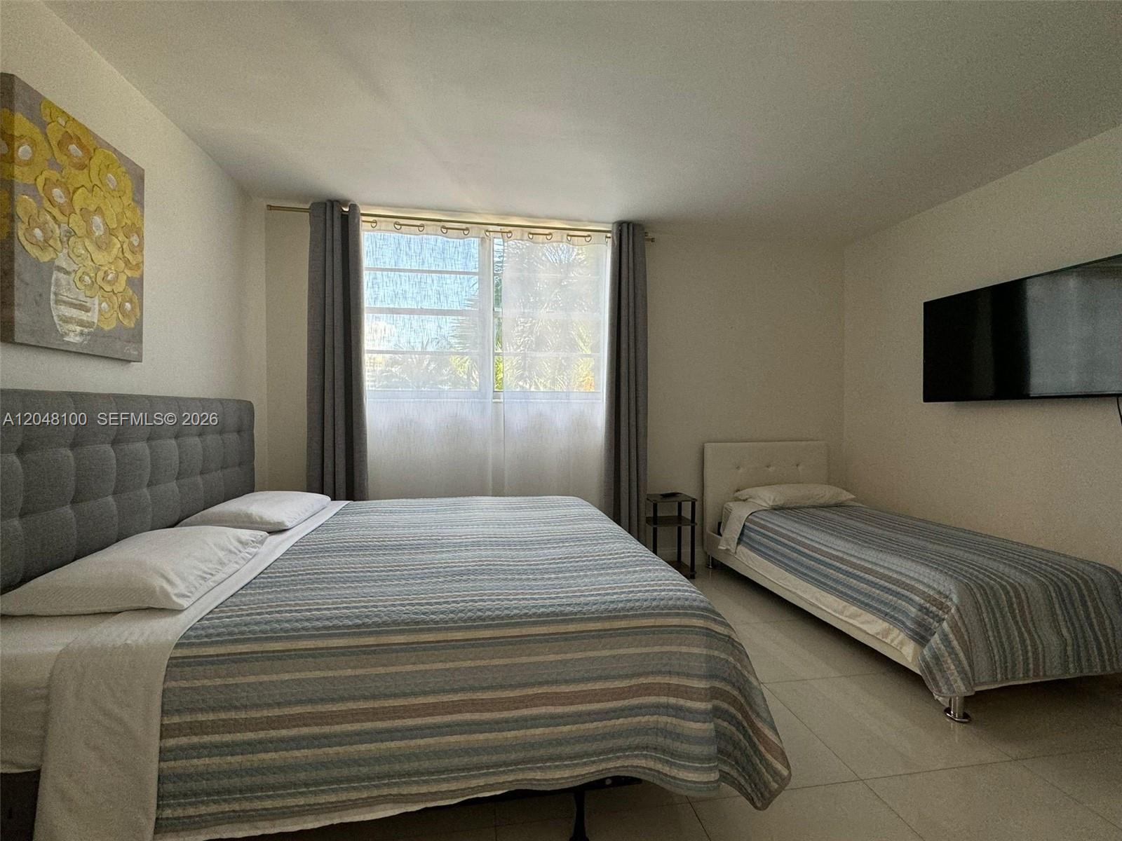 A bedroom features a queen bed, a twin bed, a wall-mounted television, and tile flooring — 3901 S Ocean Dr # 3U, Hollywood FL 33019, HOLLYWOOD, FL