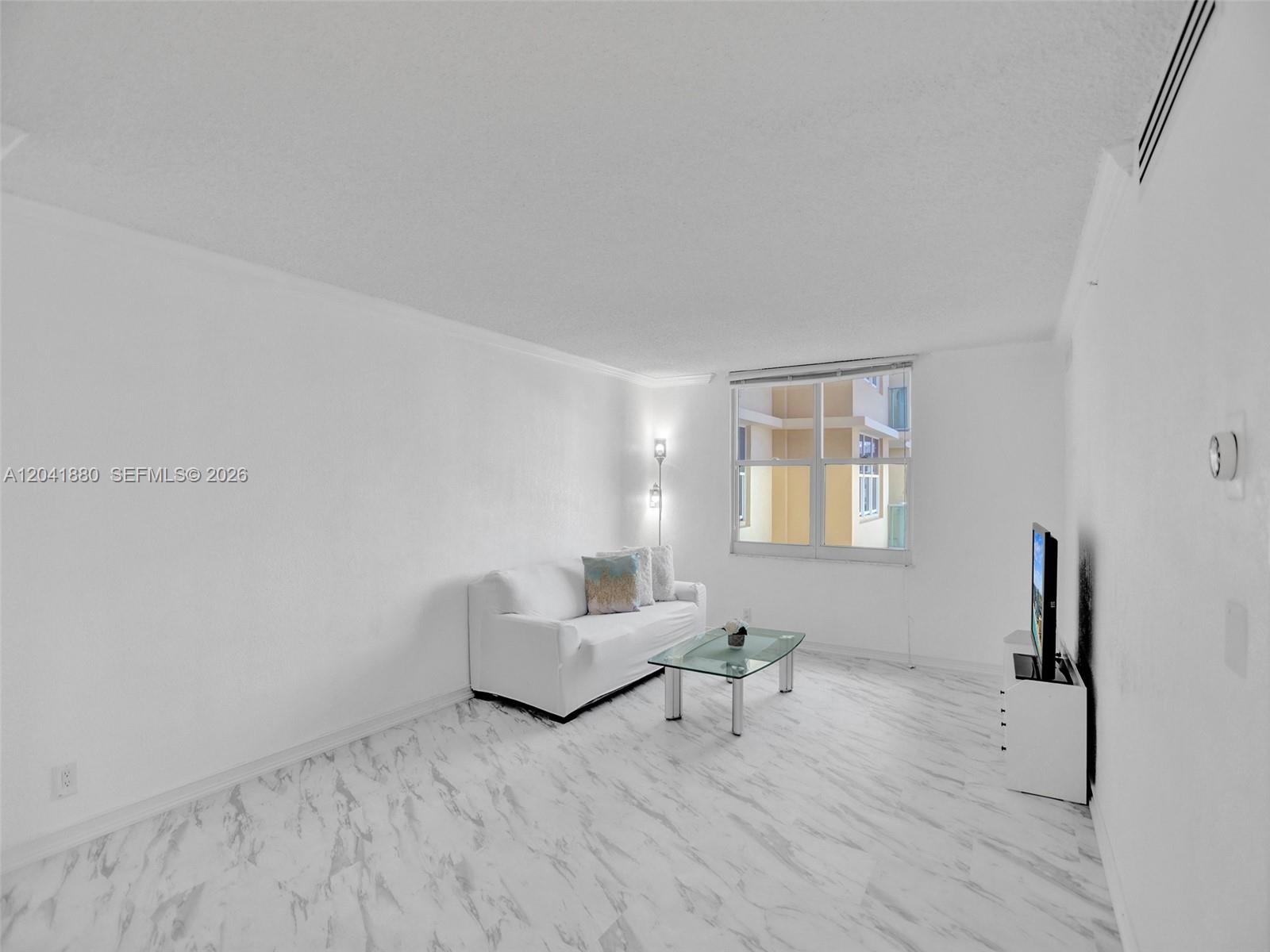 A living room features white walls, marble-patterned flooring, a white sofa, and a glass coffee table — 2501 S Ocean Dr, Hollywood FL 33019, HOLLYWOOD, FL