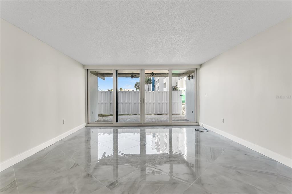 An empty room with glossy gray tile flooring and large sliding glass doors to a patio — 450 TREASURE ISLAND CAUSEWAY UNIT 104, TREASURE ISLAND, FL