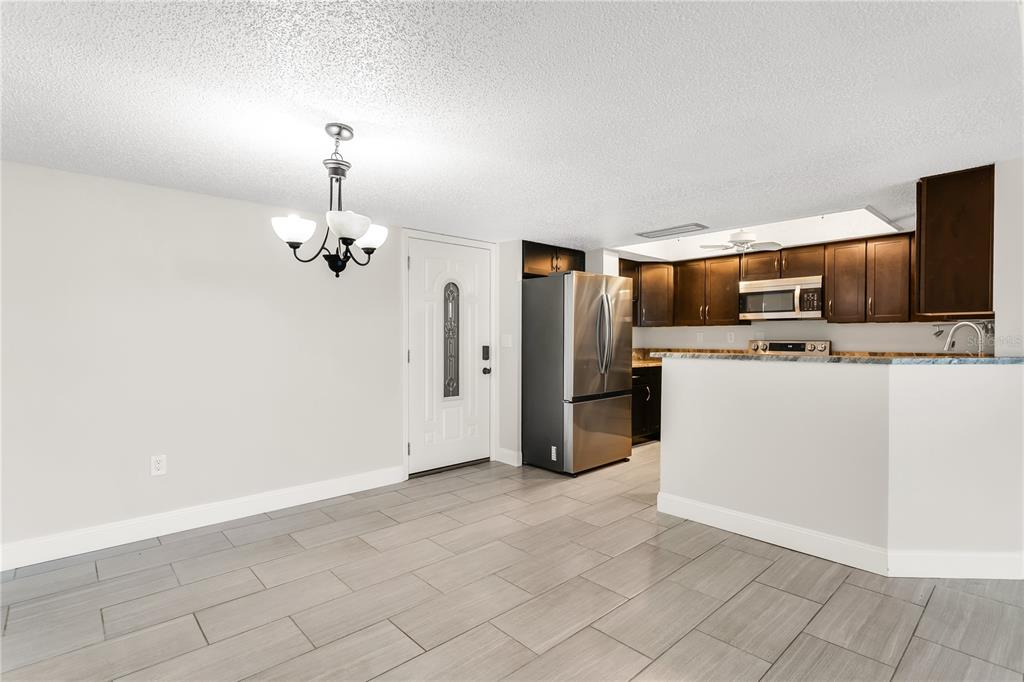 A dining area with tile floors and a chandelier adjacent to a kitchen with dark cabinets — 450 TREASURE ISLAND CAUSEWAY UNIT 104, TREASURE ISLAND, FL