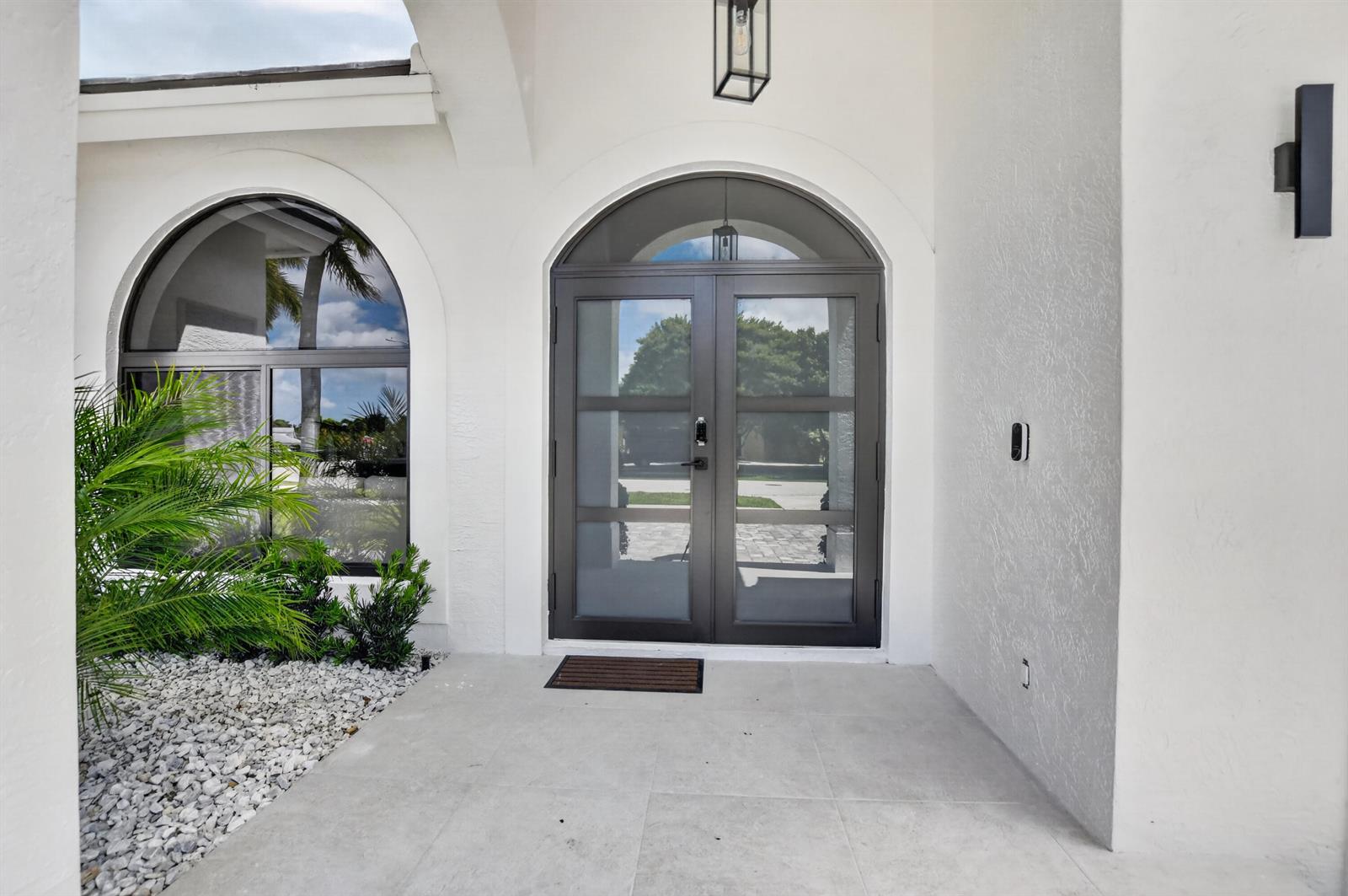 A white stucco entryway features double glass doors with an arched transom and a palm plant — 7548 Fairway Trail, Boca Raton FL 33487, BOCA RATON, FL