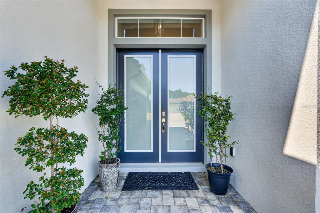 A double front door with glass panels and a transom window sits on a paved porch — 635 MAHOGANY RUN, PALM COAST, FL