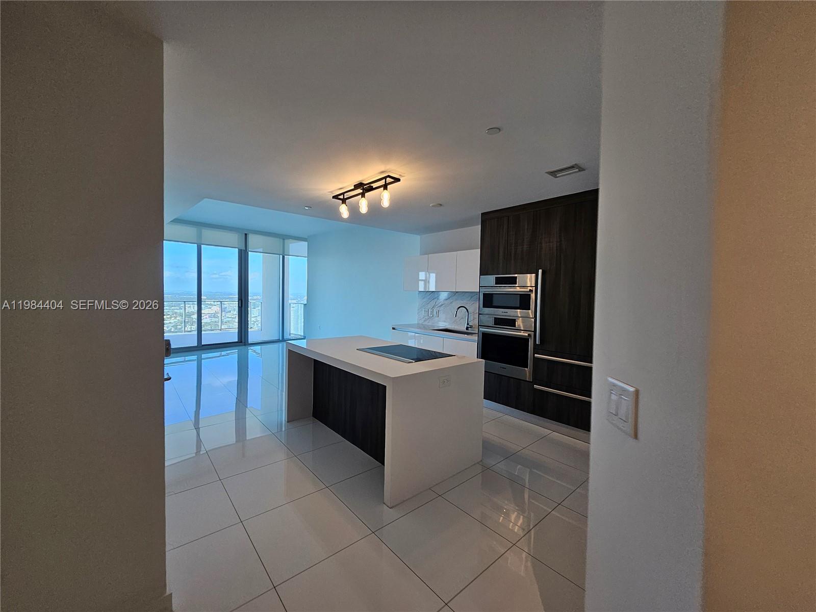 A modern kitchen features a white island, dark wood cabinetry, and floor-to-ceiling windows — 851 NE 1st Ave # 4000, Miami FL 33132, MIAMI, FL