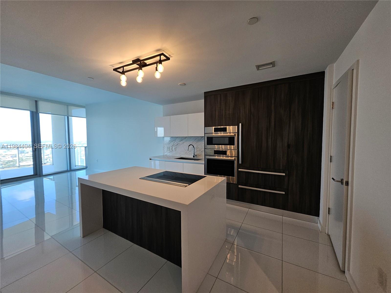 A modern kitchen features a white island, dark wood cabinetry, and large floor-to-ceiling windows — 851 NE 1st Ave # 4000, Miami FL 33132, MIAMI, FL