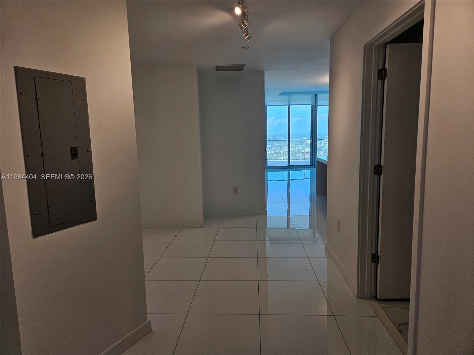 A hallway with white tile floors leads toward a room with floor-to-ceiling windows — 851 NE 1st Ave # 4000, Miami FL 33132, MIAMI, FL