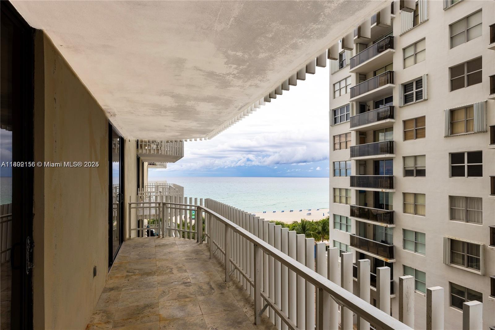 A balcony with stone flooring overlooks the ocean and an adjacent high-rise building — 6061 Collins Ave # 7D, Miami Beach FL 33140, MIAMI BEACH, FL