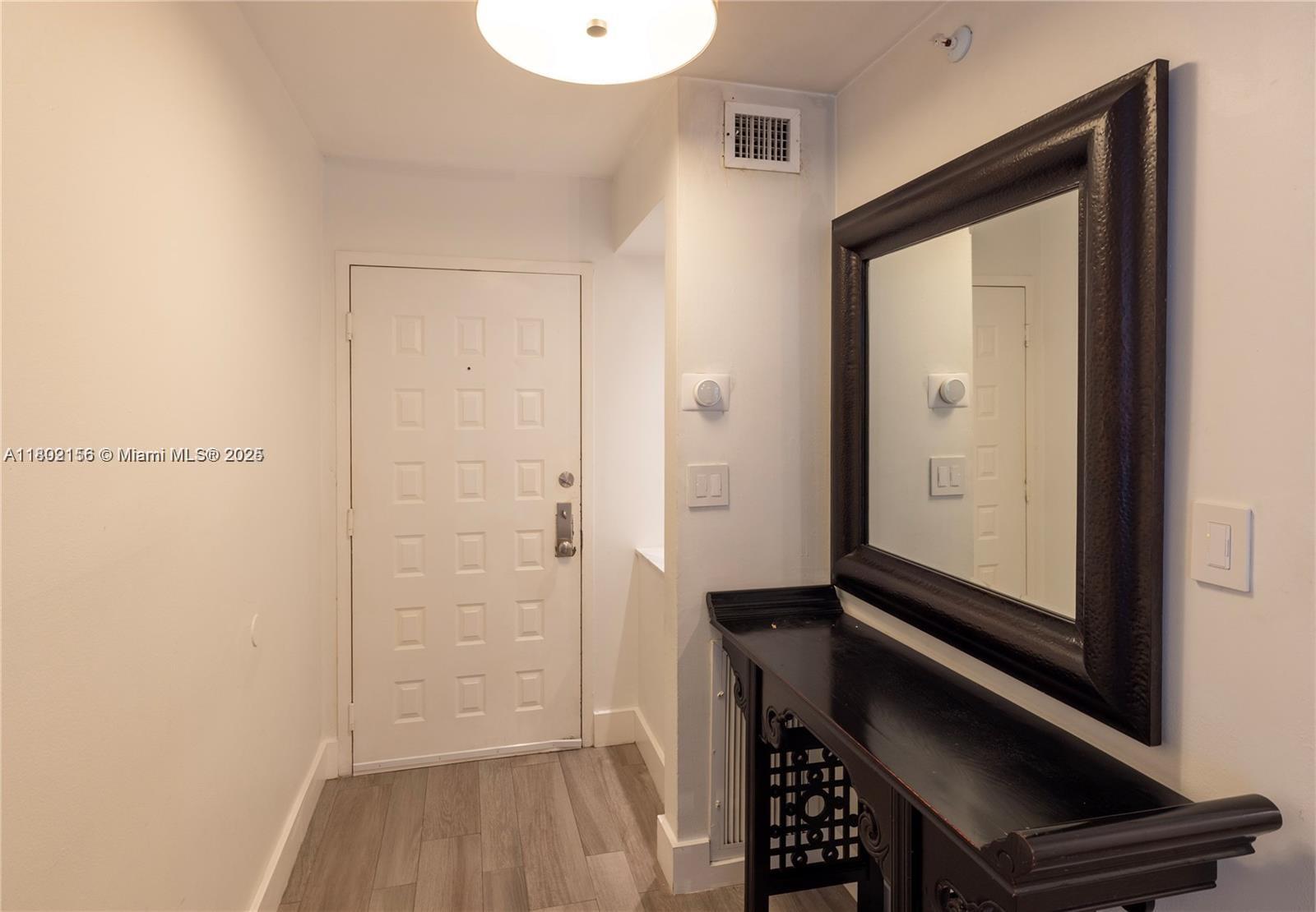 An entryway features a white door, wood-look flooring, a black console table, and a wall mirror — 6061 Collins Ave # 7D, Miami Beach FL 33140, MIAMI BEACH, FL