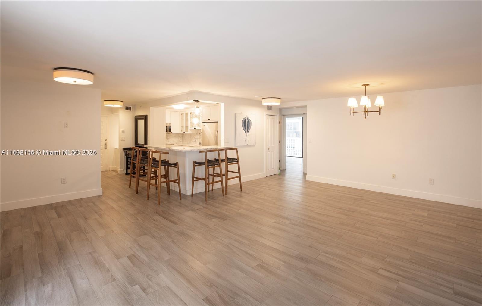 An open-concept living area features light wood flooring, a kitchen island, and a dining chandelier — 6061 Collins Ave # 7D, Miami Beach FL 33140, MIAMI BEACH, FL