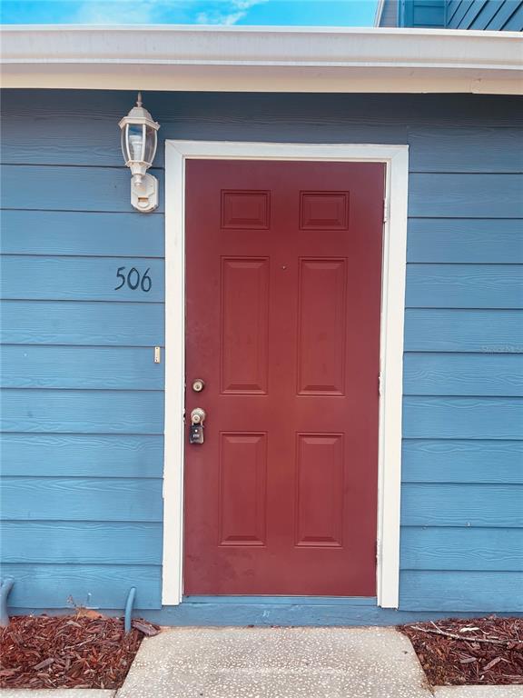 A red front door with a lockbox is set into a blue-sided exterior wall — 506 CARIBBEAN DRIVE UNIT B, DAVENPORT, FL