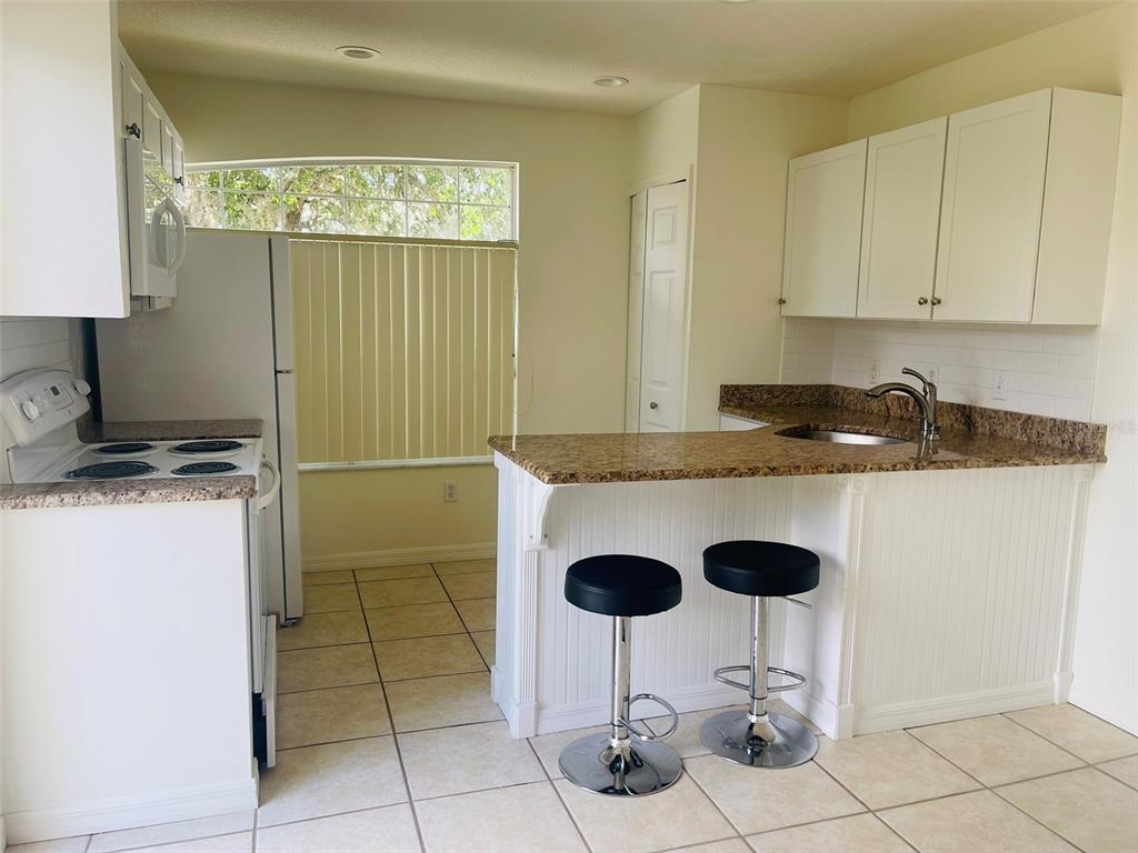 A kitchen features white cabinets, granite countertops, a breakfast bar with stools, and tile flooring — 506 CARIBBEAN DRIVE UNIT B, DAVENPORT, FL