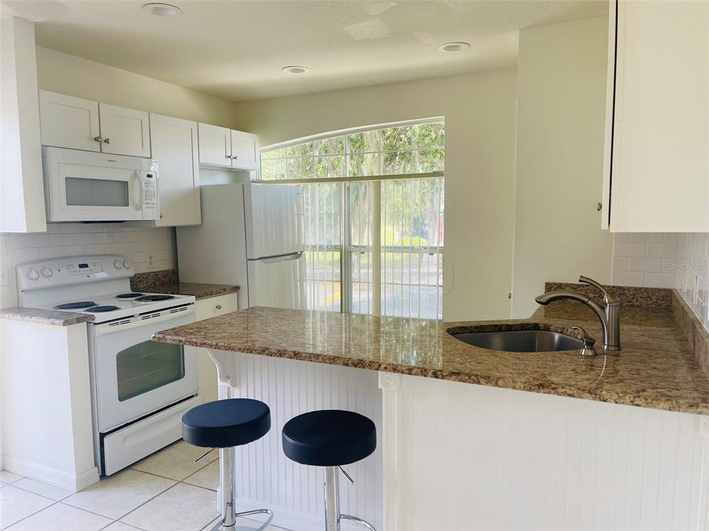 A kitchen features white cabinets, granite countertops, a breakfast bar with stools, and a window — 506 CARIBBEAN DRIVE UNIT B, DAVENPORT, FL