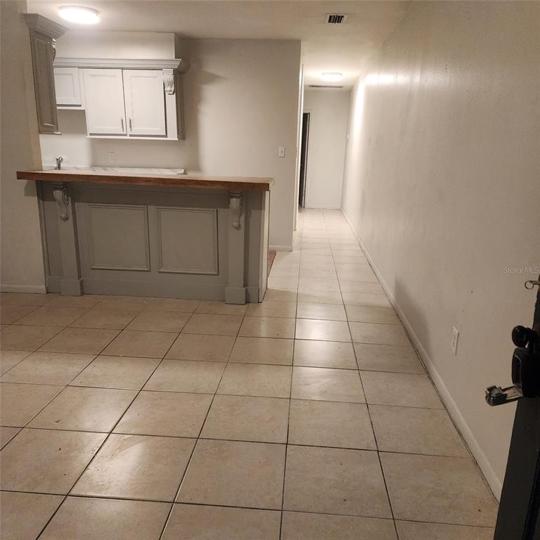 A kitchen with a breakfast bar, light-colored cabinets, and tiled flooring leads to a hallway — 1205 E 99TH AVENUE, TAMPA, FL
