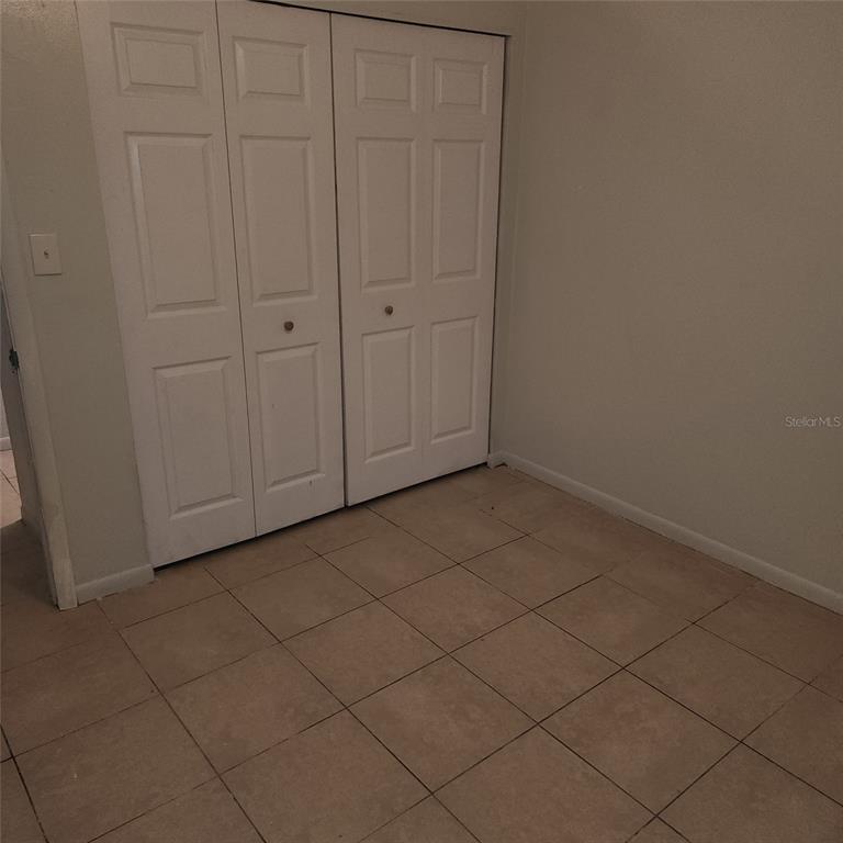 A room with light-colored tile flooring and white bi-fold closet doors — 1205 E 99TH AVENUE, TAMPA, FL