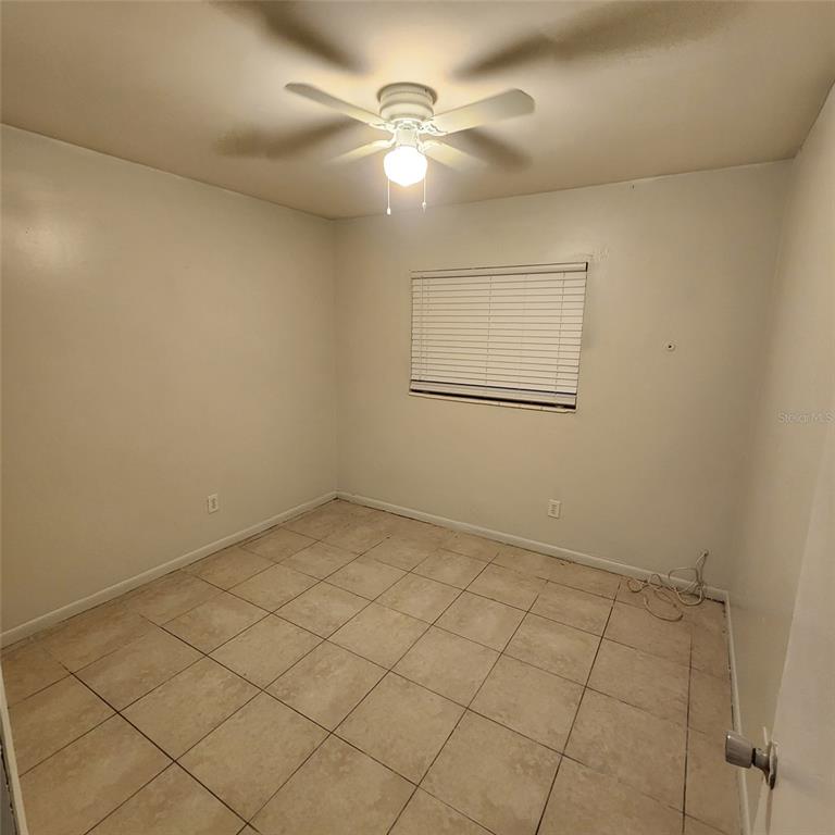 An empty room with white walls, a ceiling fan, and light-colored tile flooring — 1205 E 99TH AVENUE, TAMPA, FL