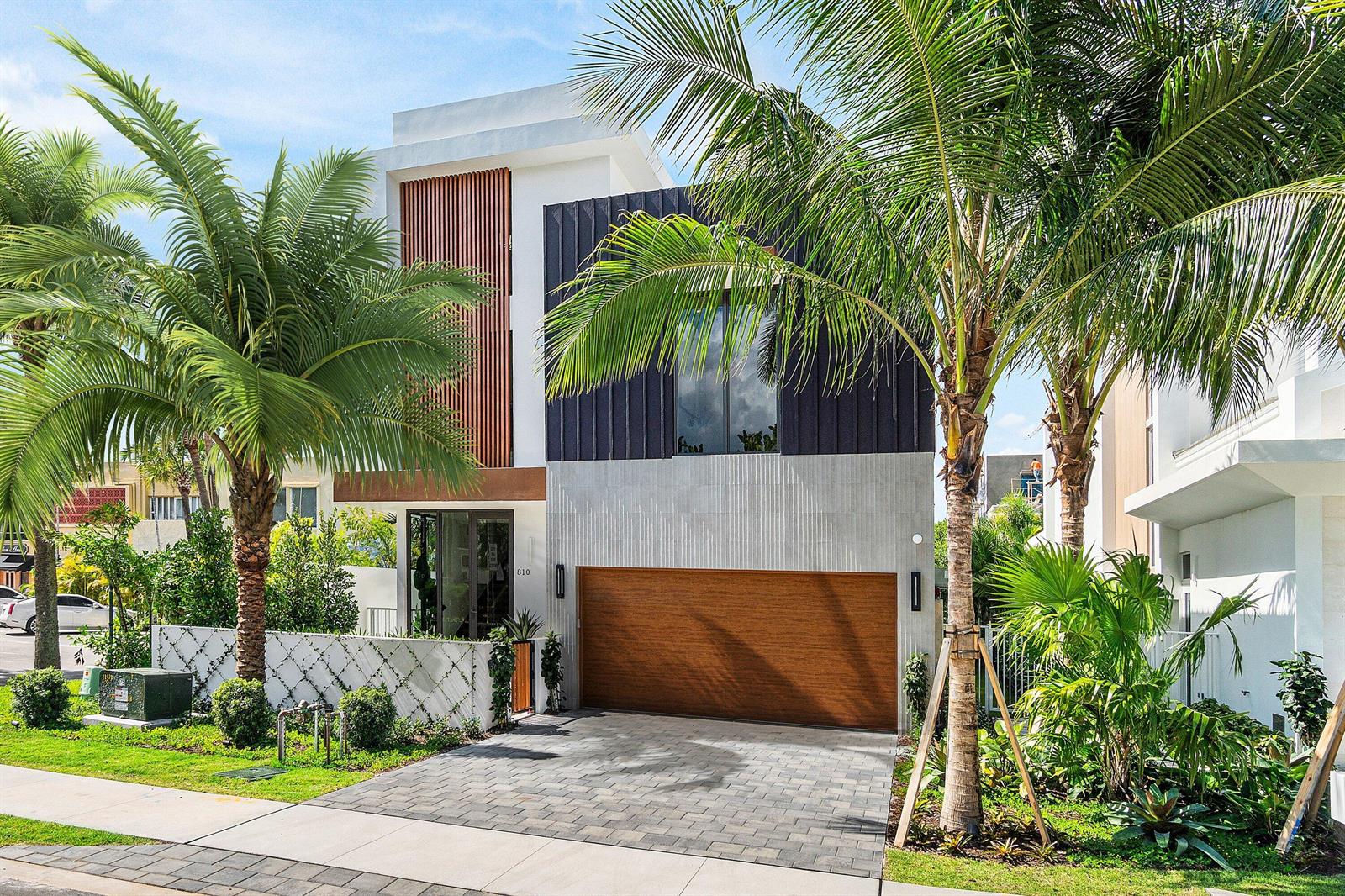A modern two-story house features a wood-paneled garage, vertical slat accents, and palm trees — 810 Palm Trail, Delray Beach FL 33483, DELRAY BEACH, FL