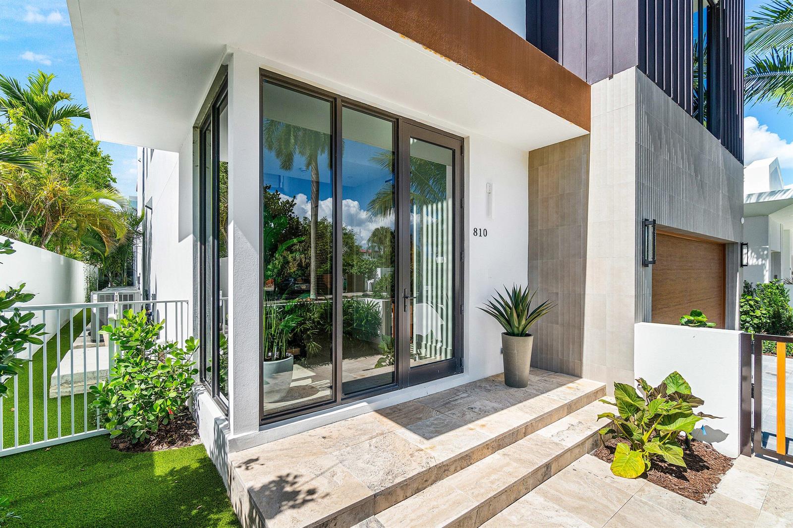 A modern home entrance features glass doors, stone steps, and a potted plant — 810 Palm Trail, Delray Beach FL 33483, DELRAY BEACH, FL