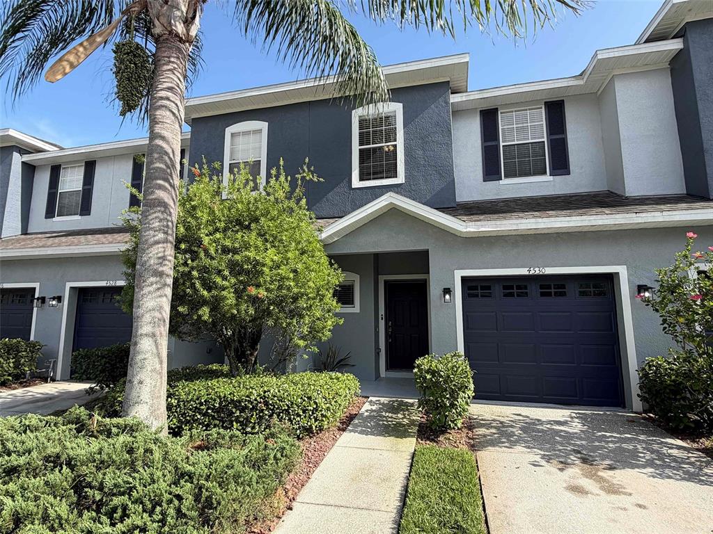 A two-story townhouse exterior features a dark blue garage door and a palm tree — 4530 AMBERLY OAKS COURT, TAMPA, FL