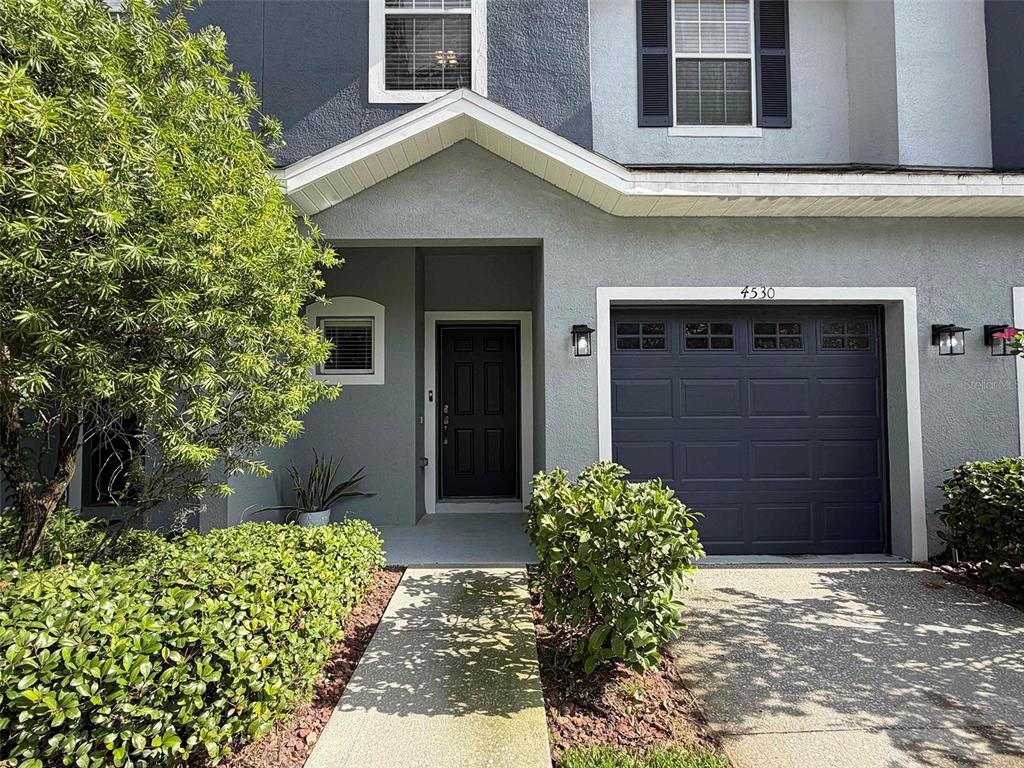 A gray two-story townhouse features a dark front door, a one-car garage, and landscaping — 4530 AMBERLY OAKS COURT, TAMPA, FL