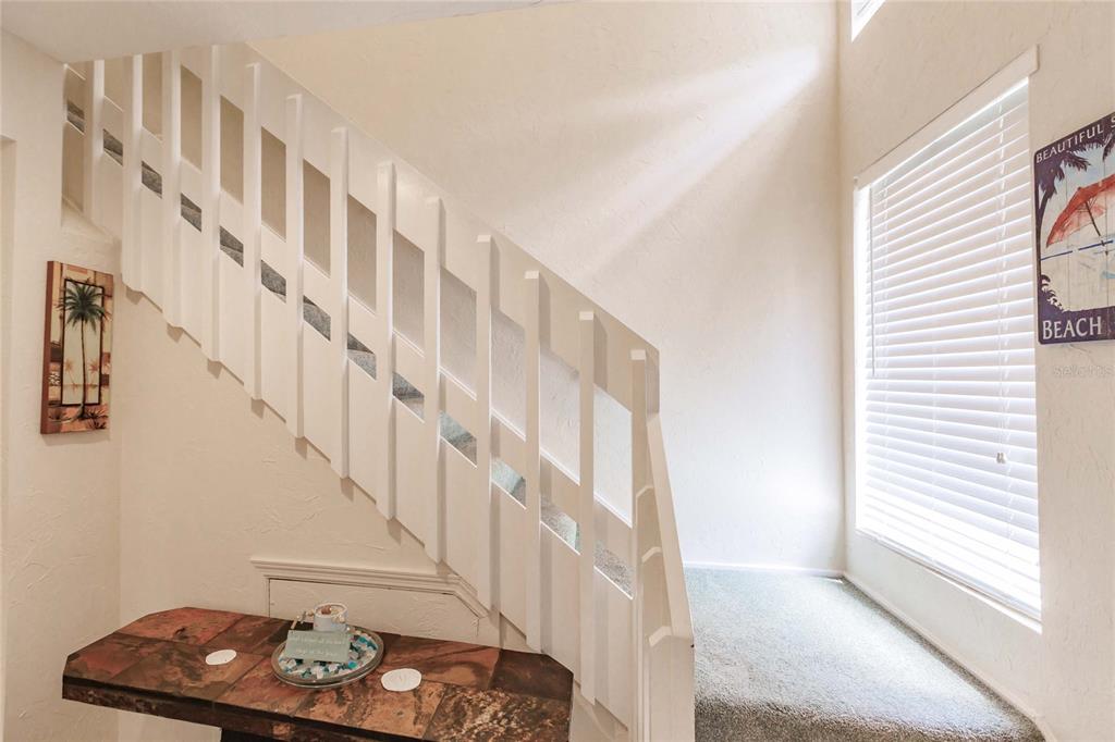 A carpeted staircase with white wooden railings sits next to a tiled entryway table — 1205 E PEPPERTREE DRIVE UNIT 232, SARASOTA, FL