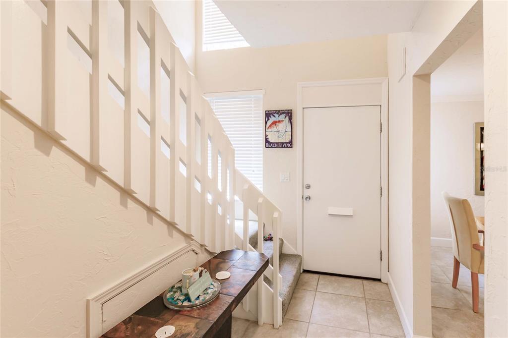 An entryway features a white staircase with a wooden console table and tiled flooring — 1205 E PEPPERTREE DRIVE UNIT 232, SARASOTA, FL