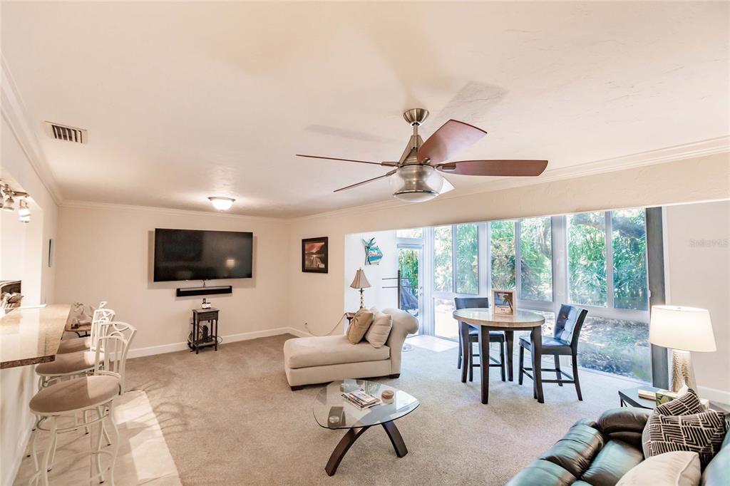 A living room features a ceiling fan, a television, a dining area, and large windows — 1205 E PEPPERTREE DRIVE UNIT 232, SARASOTA, FL