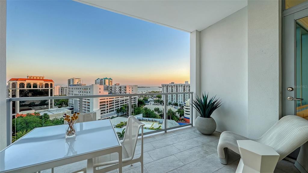 A balcony features a dining table, a lounge chair, and a view of city buildings — 111 S PINEAPPLE AVENUE UNIT 1013, SARASOTA, FL