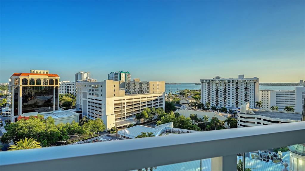 An elevated view from a balcony overlooking a city skyline, parking structures, and the ocean — 111 S PINEAPPLE AVENUE UNIT 1013, SARASOTA, FL