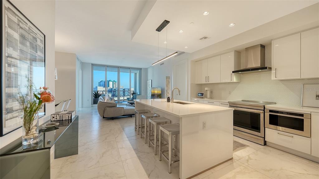 A modern kitchen with white cabinetry and a large island overlooks an open living area — 111 S PINEAPPLE AVENUE UNIT 1013, SARASOTA, FL