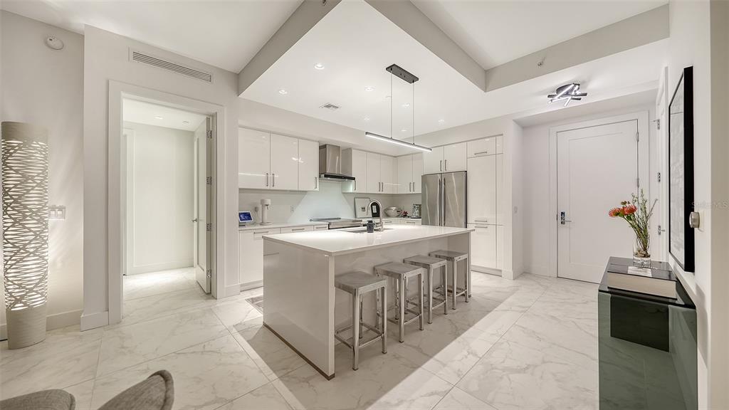A modern white kitchen features a central island with bar stools and marble flooring — 111 S PINEAPPLE AVENUE UNIT 1013, SARASOTA, FL