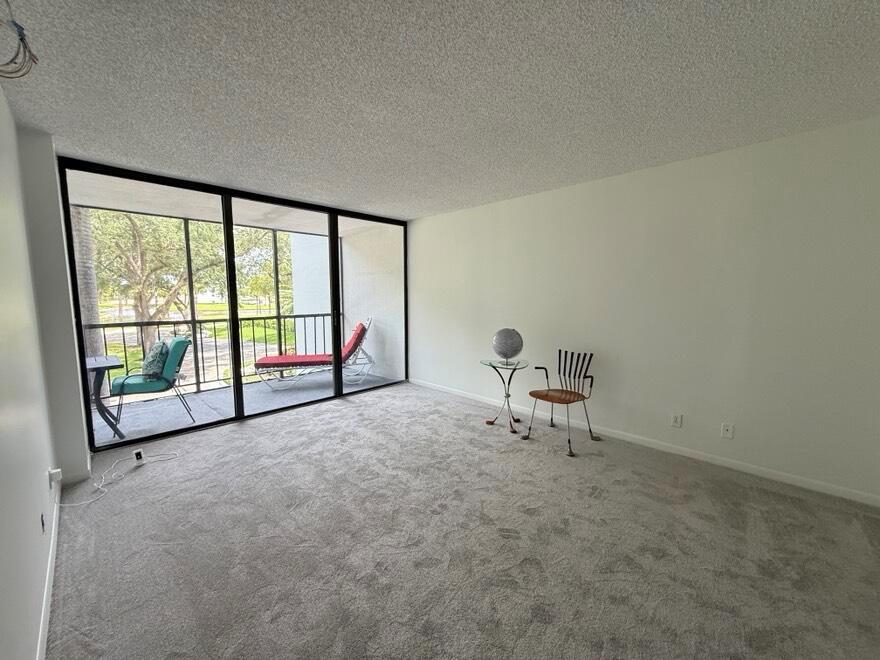 A carpeted living room features a large sliding glass door leading to a screened balcony — 7847 Lakeside Boulevard # 1024, Boca Raton FL 33434, BOCA RATON, FL