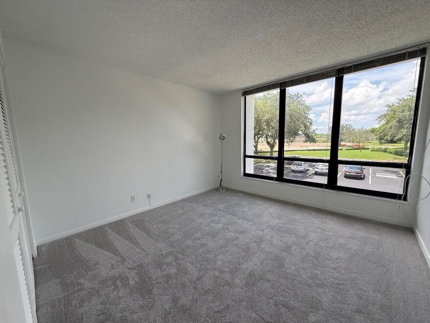 An empty bedroom features gray carpet, white walls, and a large window overlooking a parking lot — 7847 Lakeside Boulevard # 1024, Boca Raton FL 33434, BOCA RATON, FL