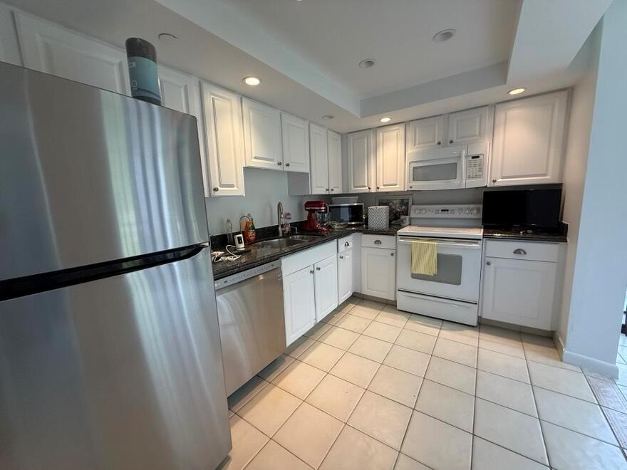 A kitchen features white cabinetry, stainless steel appliances, dark countertops, and light tile flooring — 7847 Lakeside Boulevard # 1024, Boca Raton FL 33434, BOCA RATON, FL