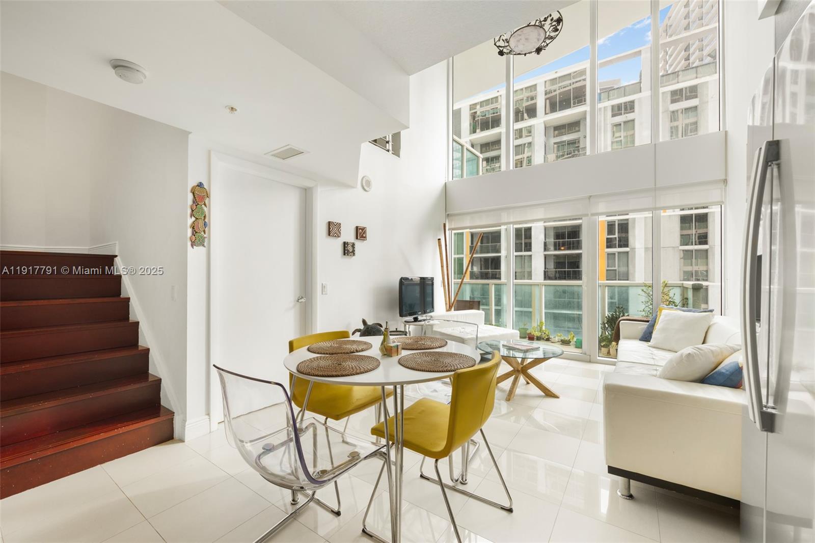 A bright living and dining area features high ceilings, floor-to-ceiling windows, and a staircase — 41 SE 5th St # 1210, Miami FL 33131, MIAMI, FL