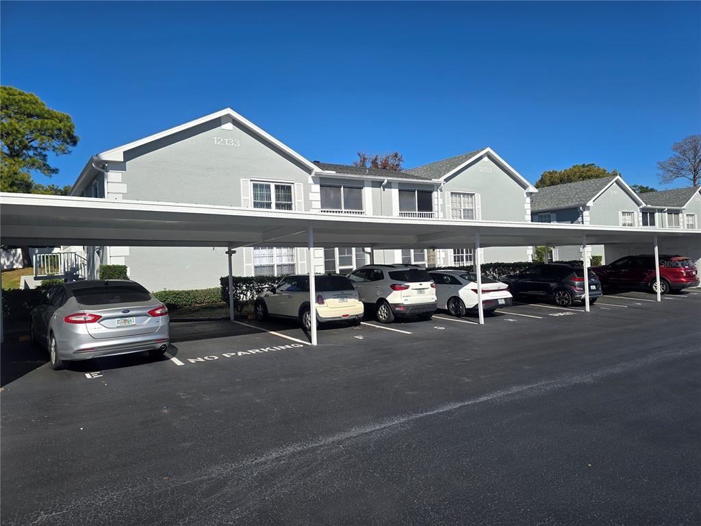 A two-story apartment building features a covered parking area with several parked cars — 12133 SPARTAN WAY UNIT 102, HUDSON, FL