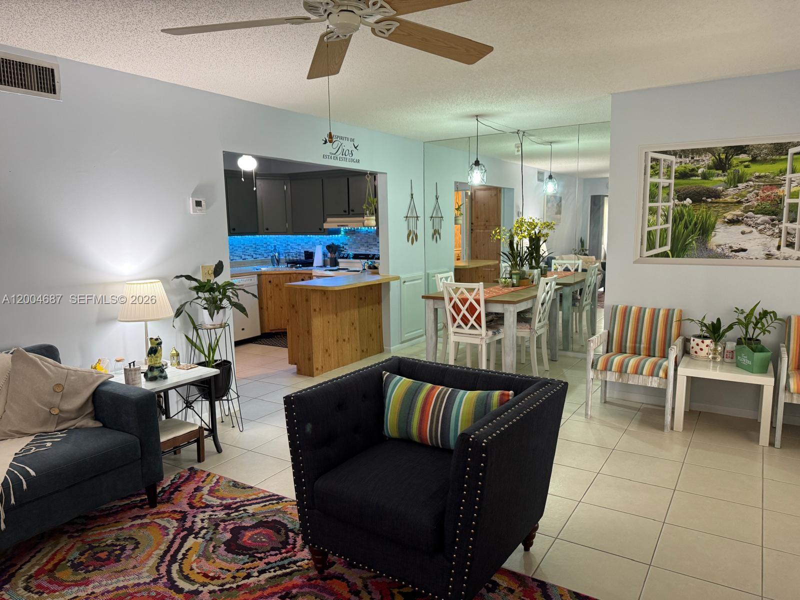 A living room with a dark armchair, patterned rug, and an open kitchen with wooden cabinets — 208 Pine Hov Cir # 2, Green Acres FL 33463, GREEN ACRES, FL