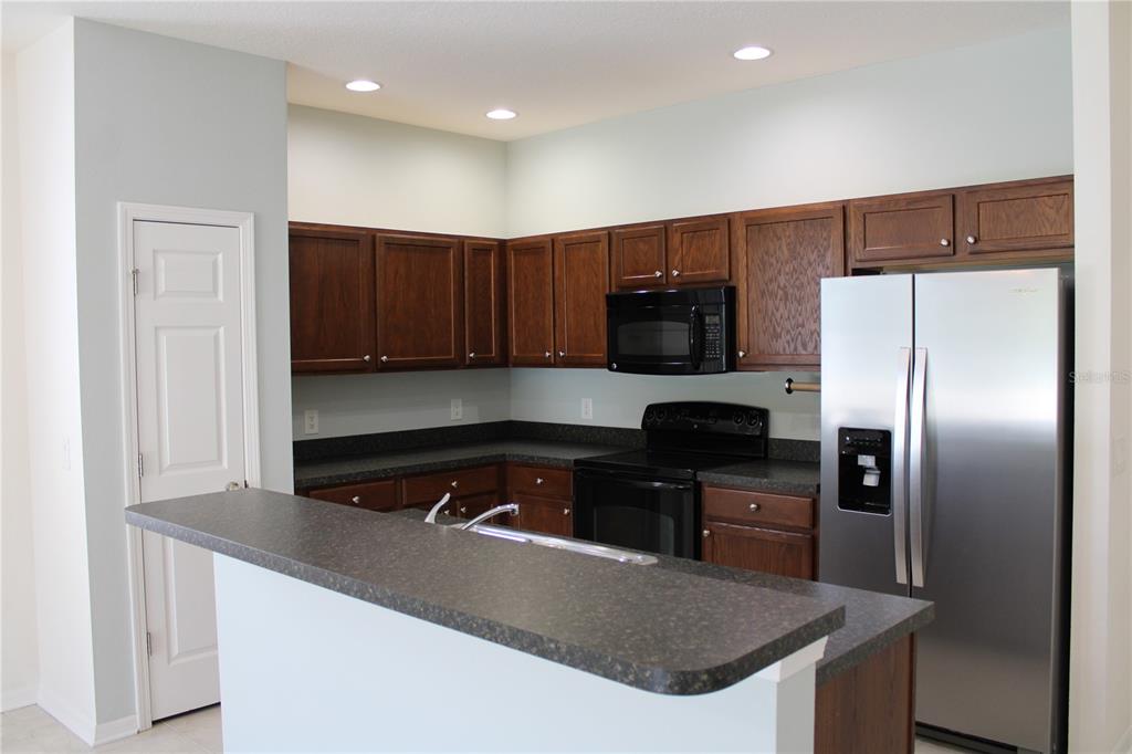 A kitchen features dark wood cabinets, black appliances, and a gray countertop breakfast bar — 5024 119TH TERRACE E, PARRISH, FL
