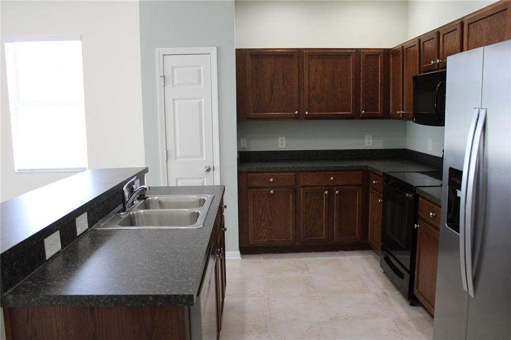 A kitchen features dark wood cabinets, black countertops, stainless steel appliances, and tile flooring — 5024 119TH TERRACE E, PARRISH, FL